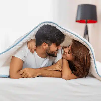 Couple cuddling under a blanket, showing what is the purpose of a honeymoon bonding time