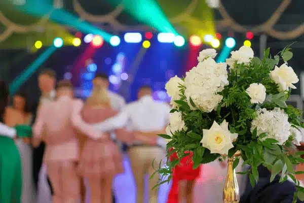 White flower arrangement in focus with blurred dancing guests and colorful stage lights in background