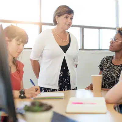 Manager leads team meeting around table in bright office, encouraging discussion, feedback, and collaboration today