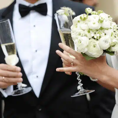 Bride and groom clink champagne glasses, display bouquet and rings during joyful wedding celebration together
