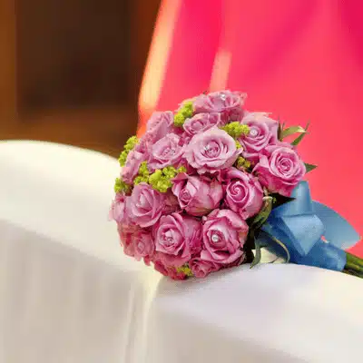 Close-up pink rose bridal bouquet with blue ribbon resting on table during wedding ceremony indoors