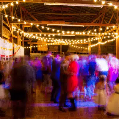Guests dance beneath string lights during barn reception; are barn weddings still popular today? debated