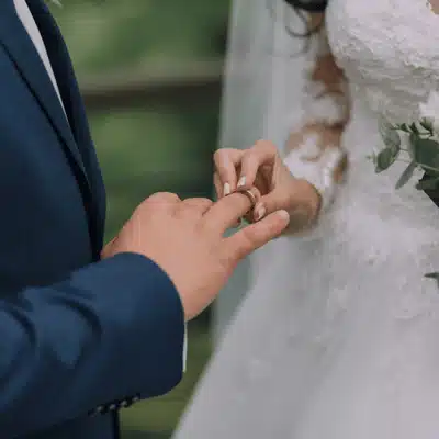 Bride places wedding ring onto groom's finger during outdoor ceremony, close-up photo capturing vows moment