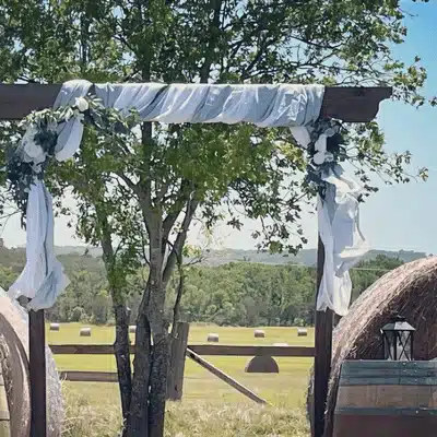 Rustic wooden arch with white draping and greenery set in pasture for venue walkthrough wedding planning
