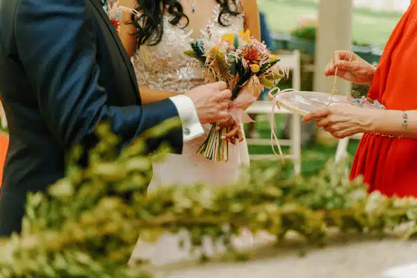 Close-up of couple holding bouquet during outdoor ceremony while officiant prepares rings and vows today