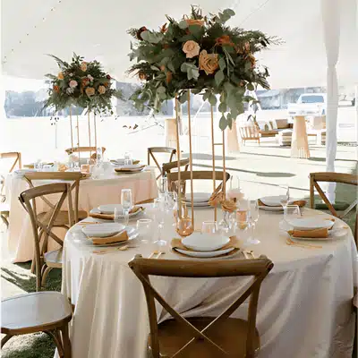 Elegant tented wedding reception setup with round tables, glassware, blush linens, and tall floral centerpieces