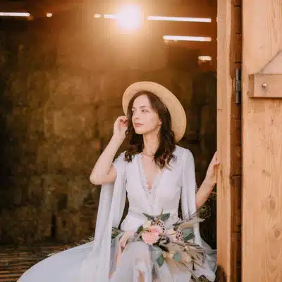 Photo shows bride in hat by rustic barn doorway, showcasing ranch wedding venues in texas