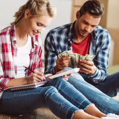 Couple seated on floor counting cash and writing budget for affordable ranch wedding venues planning