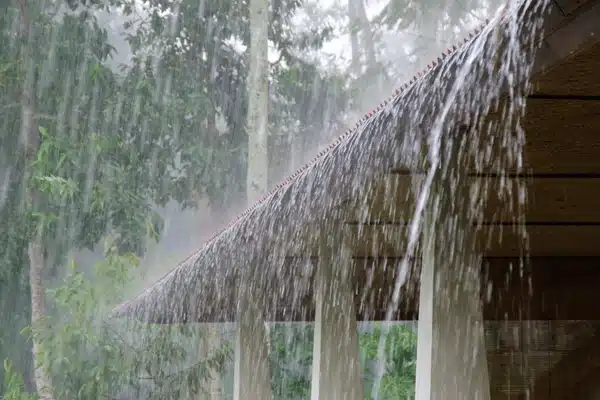 Heavy rain pours off roof eaves at wedding venue central texas, stormy trees background behind